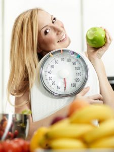 Girl with scale and fruits in the kitchen is proud to lose weigh